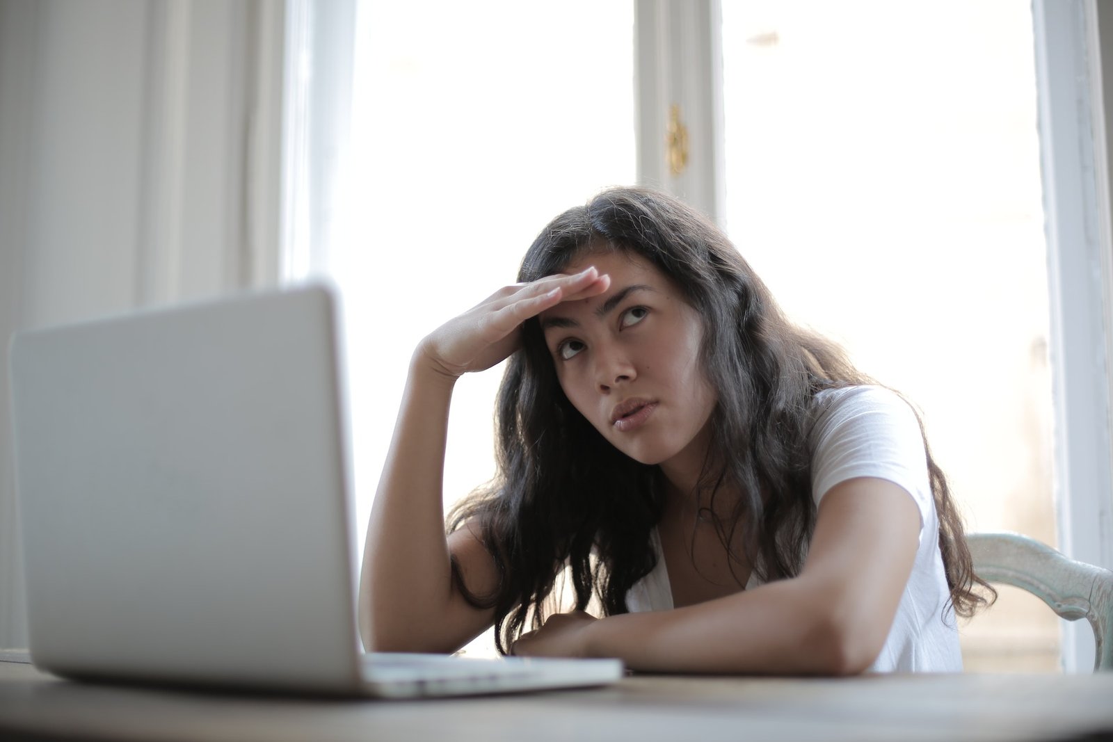 A woman with loose long dark hair sits at her laptop looking discouraged
