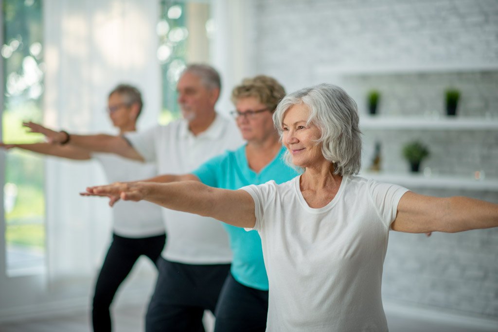 Middle-aged women and men smiling and practicing qigong in a studio