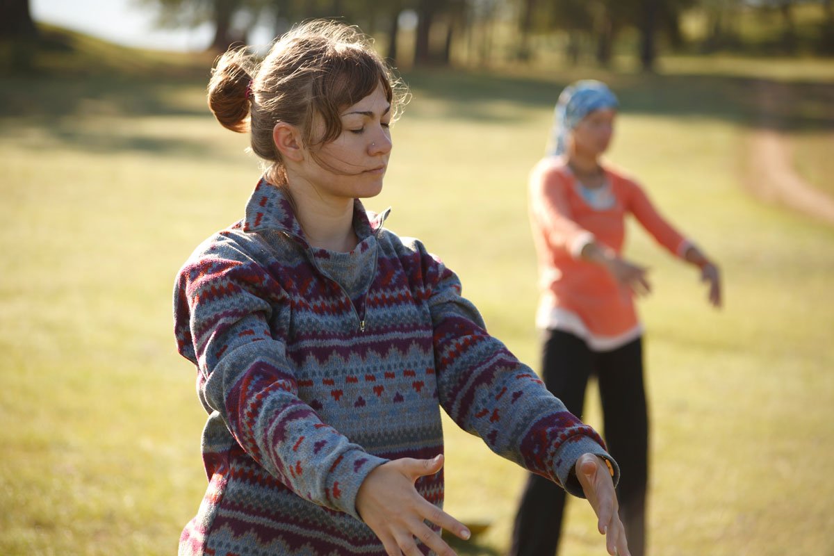 Two young women practice qigong outside. They have their eyes closed and look peaceful.